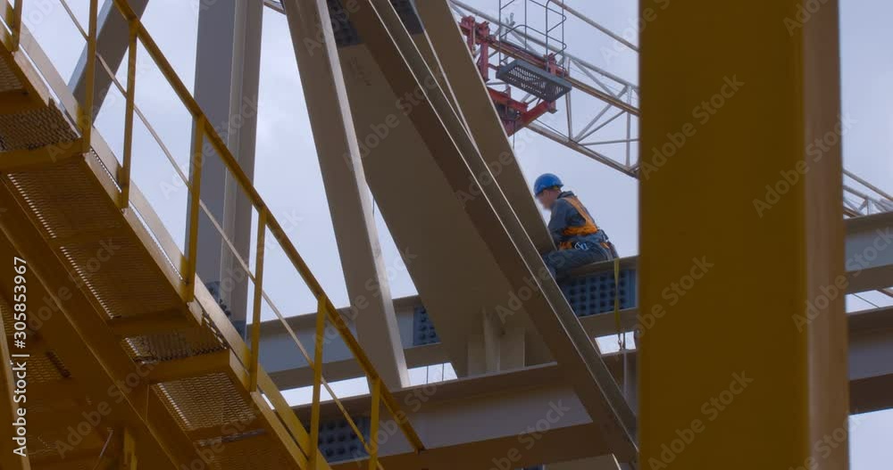 The builder works at height during the construction of the roof of the new stadium on the background of a moving crane The builder works at height during the construction of the roof of the new stadium on the background of a moving crane