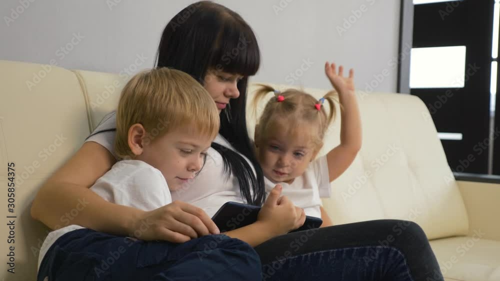 Happy family. Mom with children sits on a sofa with a computer tablet. Family watching a movie. Parenting concept. Teamwork