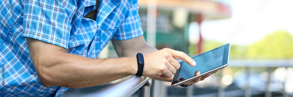 Focus on male hands with stylish fitness bracelet holding gadget and surfing internet via special app. Electronic technology concept. Blurred background