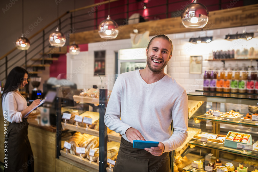 Bearded businessman holding tablet smiling while owning bakery with wife