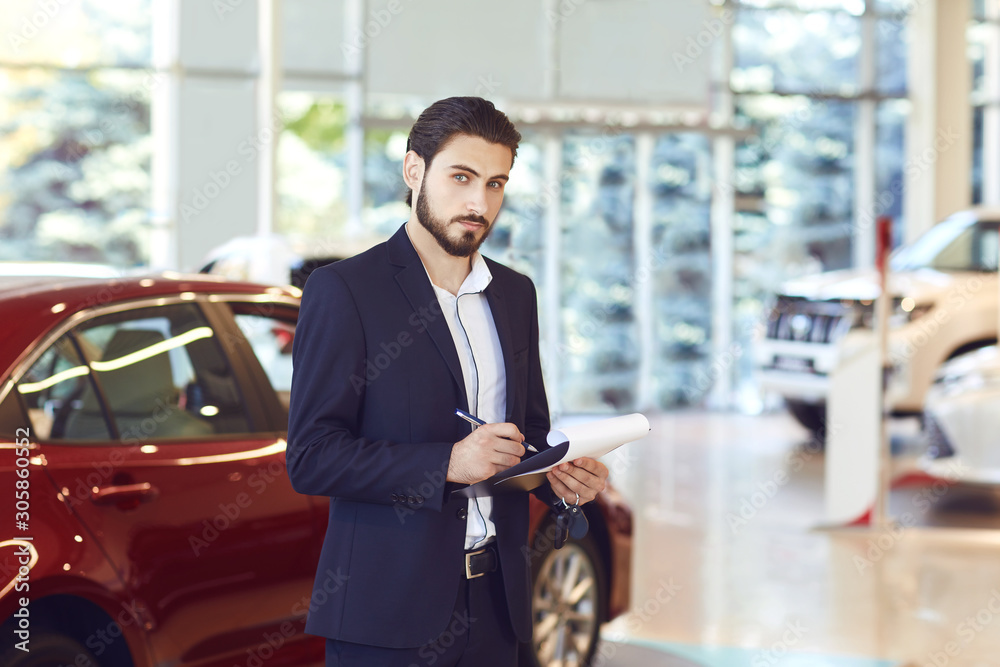 A car dealer standing in a showroom. A car dealer standing in a showroom.