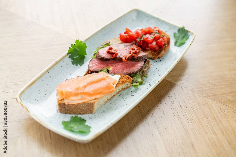 Bruschetta with beef, tomatoes and salmon. Various snacks and antipasti on the table. Restaurant menu. Italian cuisine Bruschetta with beef, tomatoes and salmon. Various snacks and antipasti on the table. Restaurant menu. Italian cuisine