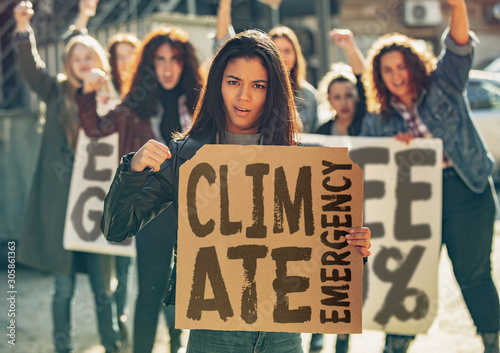 Young woman with poster in front of people protesting about climate changing on the street. Meeting about problem in ecology, environment, global warming, industrial influence, climate emergency. © master1305