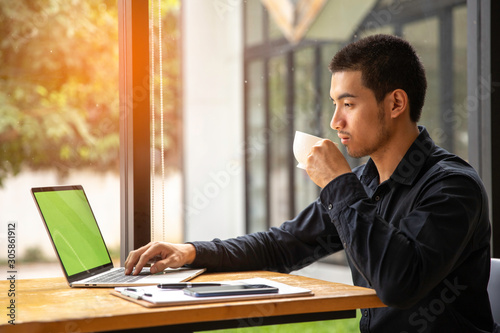 Young businessman drinking coffee and working on laptop in a cafe photo