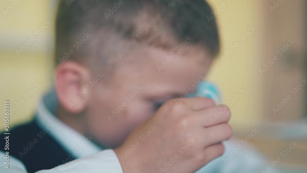 cute schoolboy in vest plays with modern spinner putting toy on nose at break in classroom closeup