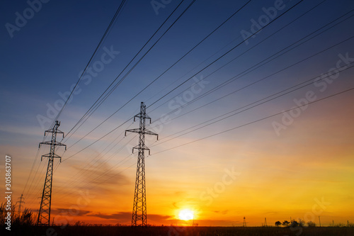 Power lines at sunset, sun rays. High voltage tower against the sky