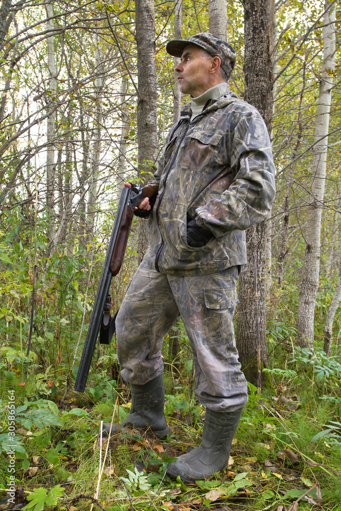 a hunter with a discharged gun stands in the thicket of aspen