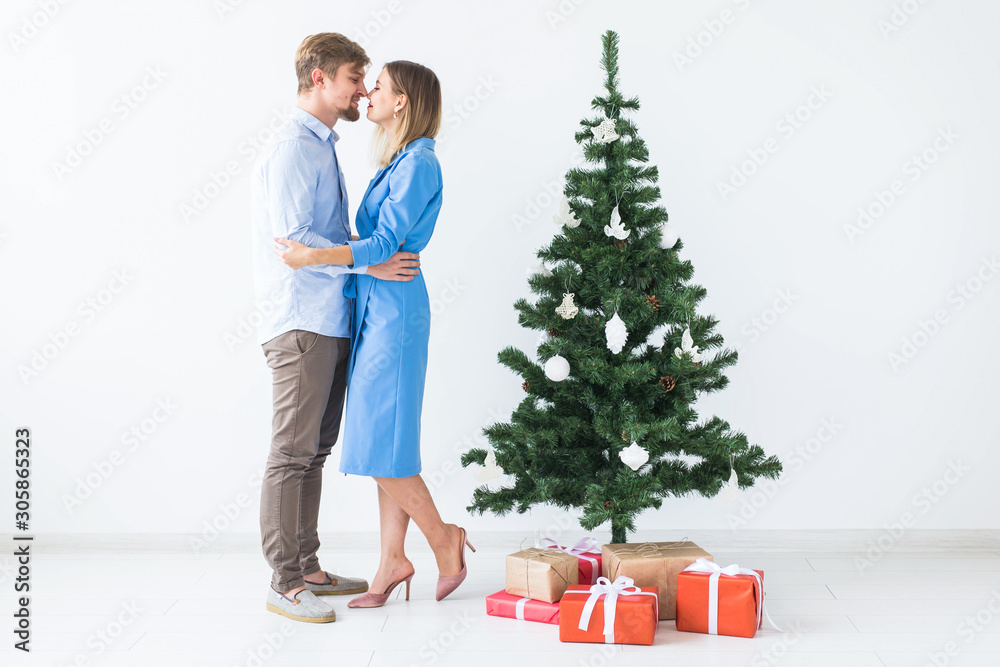 Holidays and festive concept - Young happy couple near a Christmas tree on white background Holidays and festive concept - Young happy couple near a Christmas tree on white background