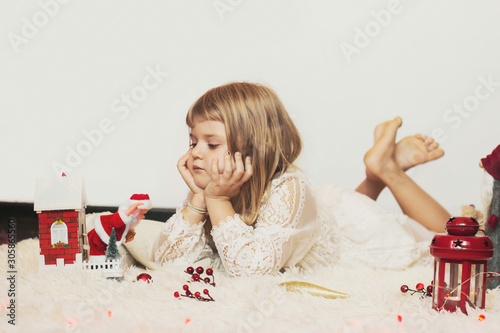 Little girl laying on the floor, playing with Christmas decoration; Christmas background with copy space