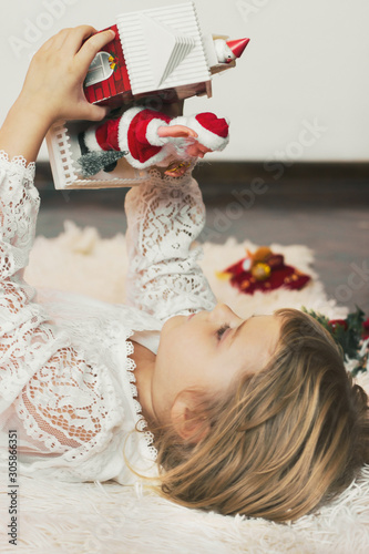 Cute little girl laying on the floor, playing with Christmas decoration, little Santa Claus coming out of the box