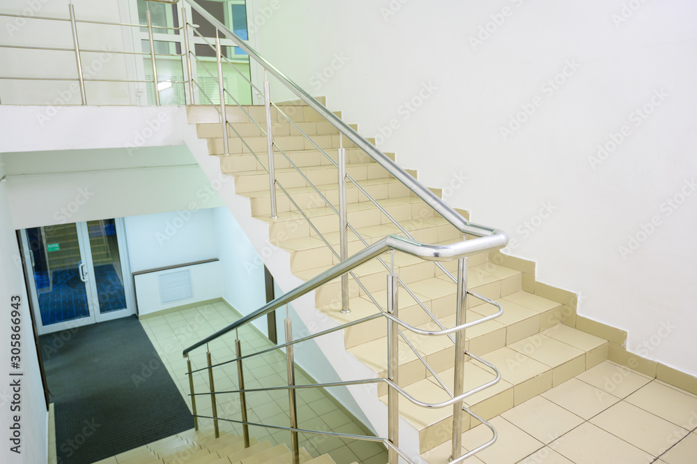 Fototapeta premium The concept of the interior of an urban building. Photo of a staircase with metal railing between floors.