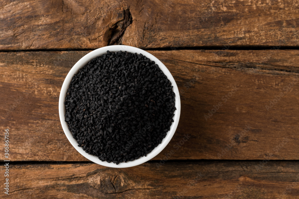Black cumin seeds in bowl on rustic wooden table. Top view Black cumin seeds in bowl on rustic wooden table. Top view