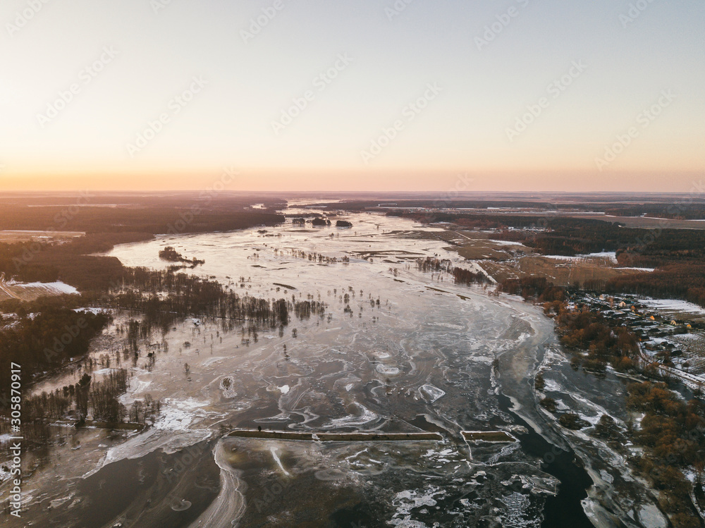 Obraz premium Winter landscape on the river with a forest among snow with a bird's-eye view. Winter sunrise