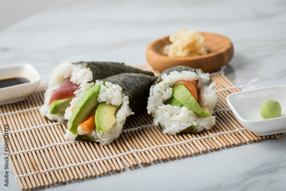 Lachs Fisch, Tunfisch und Surimi Avocado Temaki Sushi, eingelegter Ingwer mit Soja Soße und Sushimatte auf Marmor Hintergrund Lachs Fisch, Tunfisch und Surimi Avocado Temaki Sushi, eingelegter Ingwer mit Soja Soße und Sushimatte auf Marmor Hintergrund