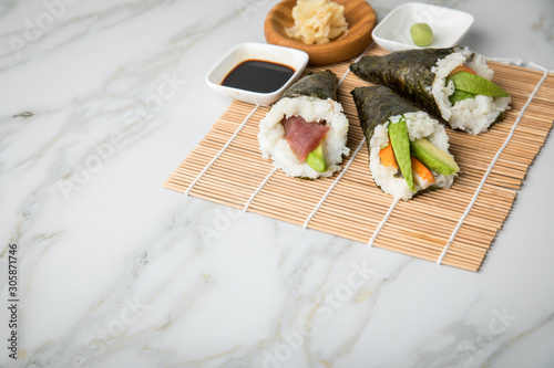 Lachs Fisch  Tunfisch und Surimi Avocado Temaki Sushi  eingelegter Ingwer mit Soja So  e und Sushimatte auf Marmor Hintergrund