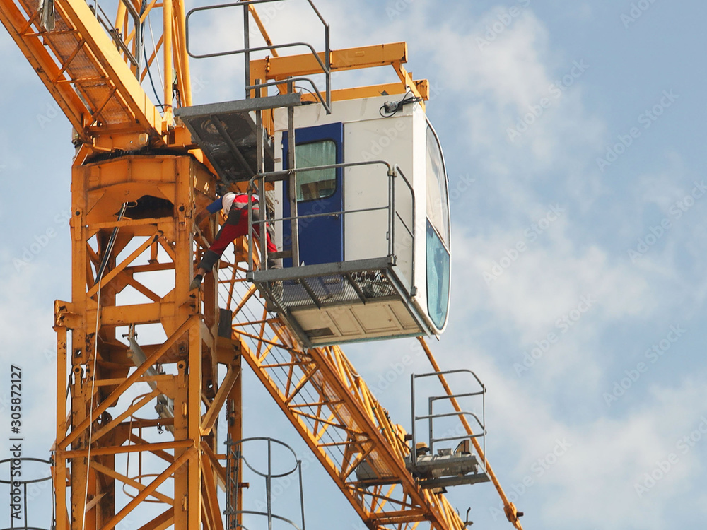 Crane workers in overalls are repairing a high-rise tower crane working during the construction of a multi-storey building. Risky work at height. Lifting heavy building materials. City development. Crane workers in overalls are repairing a high-rise tower crane working during the construction of a multi-storey building. Risky work at height. Lifting heavy building materials. City development.