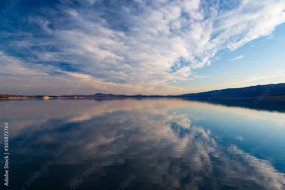 Cumulus clouds on blue sky reflecting at water of Baikal lake after sunset in May Cumulus clouds on blue sky reflecting at water of Baikal lake after sunset in May