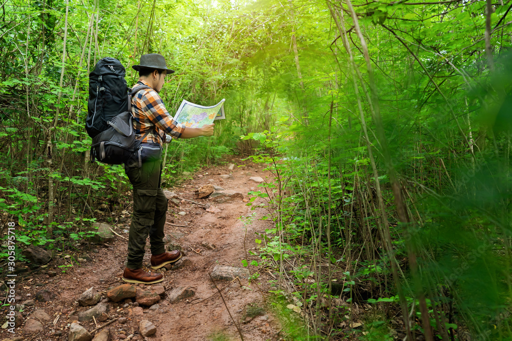 Naklejka premium man traveler with backpack and map searching directions in the forest