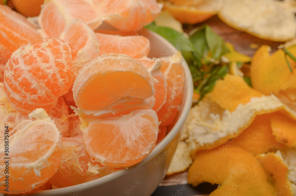 Peeled tangerines in a ceramic dish, tangerine peel on a wooden background. Autumn harvest. Close up. Peeled tangerines in a ceramic dish, tangerine peel on a wooden background. Autumn harvest. Close up.