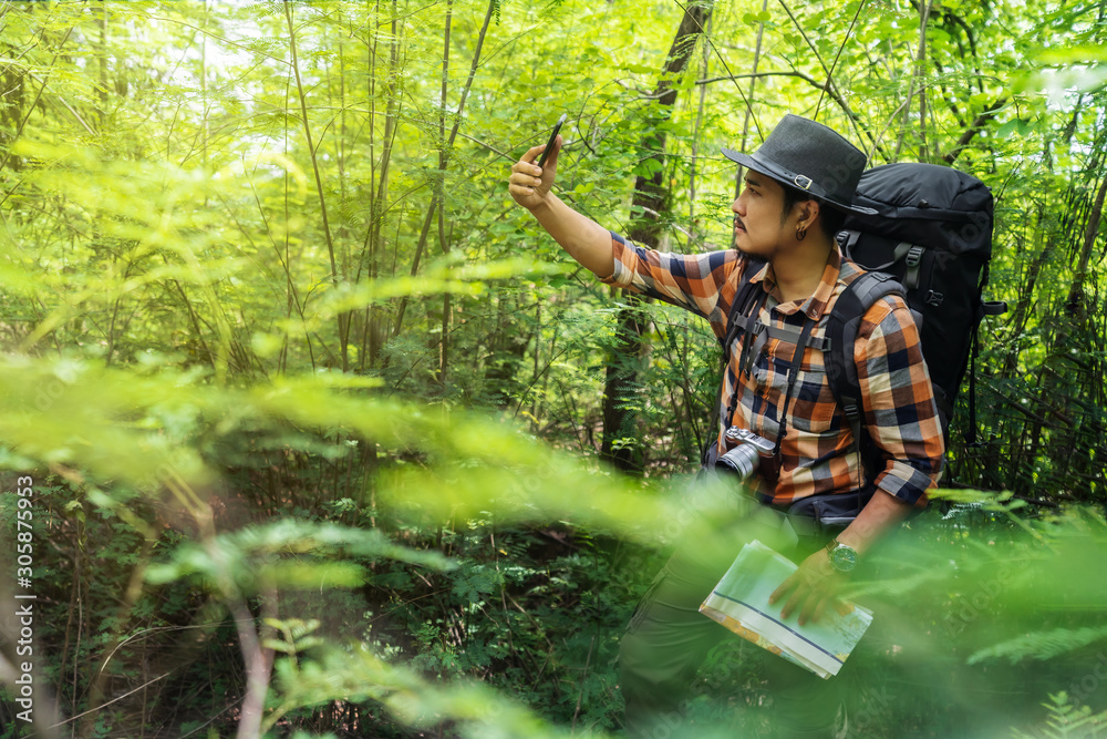 man traveler with backpack using smartphone to taking a selfie in the forest