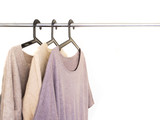 Knitted Sweaters and cardigans in beige grey neutral tone hanging  in wardrobe. Fall winter season cloth concept.