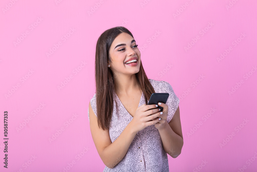 Adorable girl with mobile phone in hand expressing positive emotions. Attractive woman in pink shirt holding smartphone and texting on studio pink background Adorable girl with mobile phone in hand expressing positive emotions. Attractive woman in pink shirt holding smartphone and texting on studio pink background