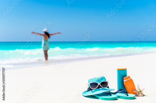 Suncream bottles  sunglasses  flip flop on white sand background ocean