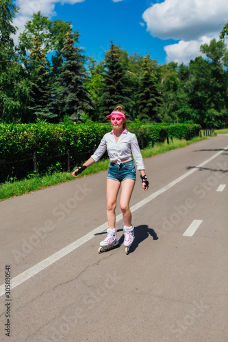 Portrait of an emotional girl in a pink cap visor and protective gloves for rollerblades and skateboarding riding on rollerblades on the road.