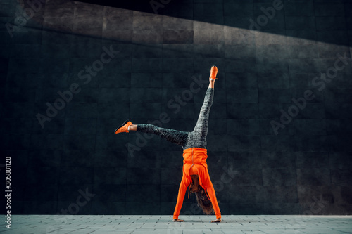 Full length of fit sporty caucasian woman in sportswear doing cartwheel exercise in front of black wall.