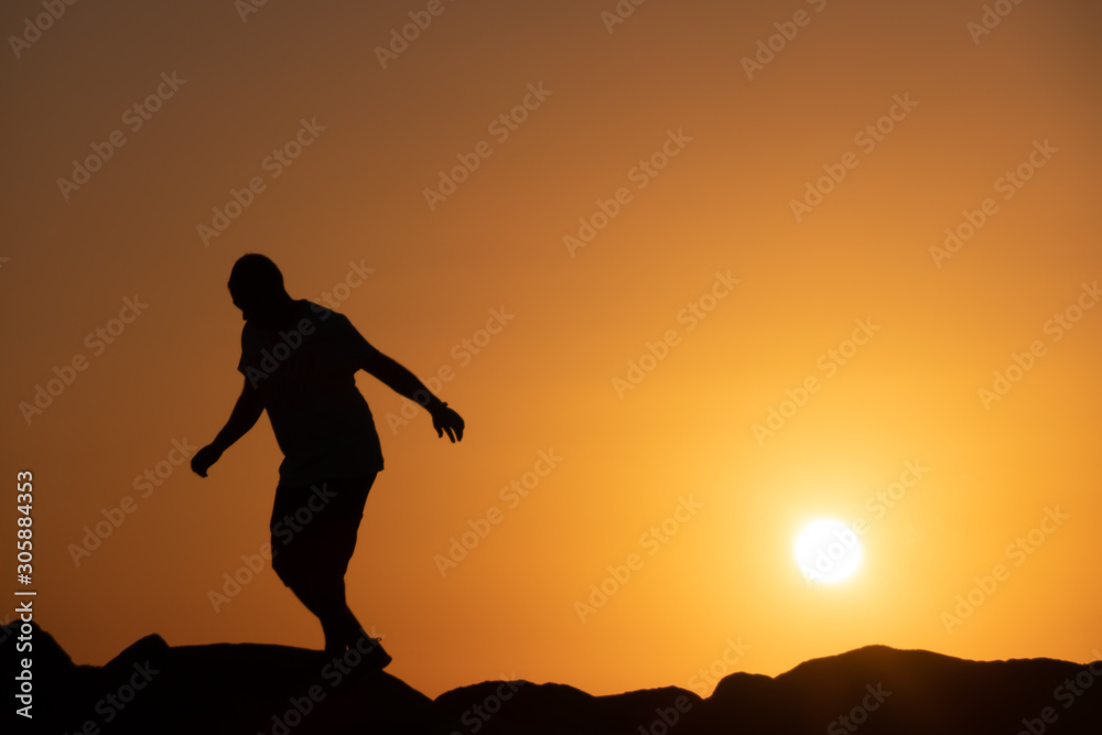 Man silhouette walking .on rocks, .orange sky at sunset. Man silhouette walking .on rocks, .orange sky at sunset.