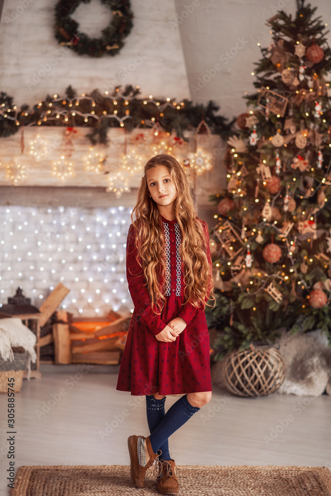  A girl near the Christmas tree. Beautiful child decorates a Christmas tree. Portrait of a girl with long hair