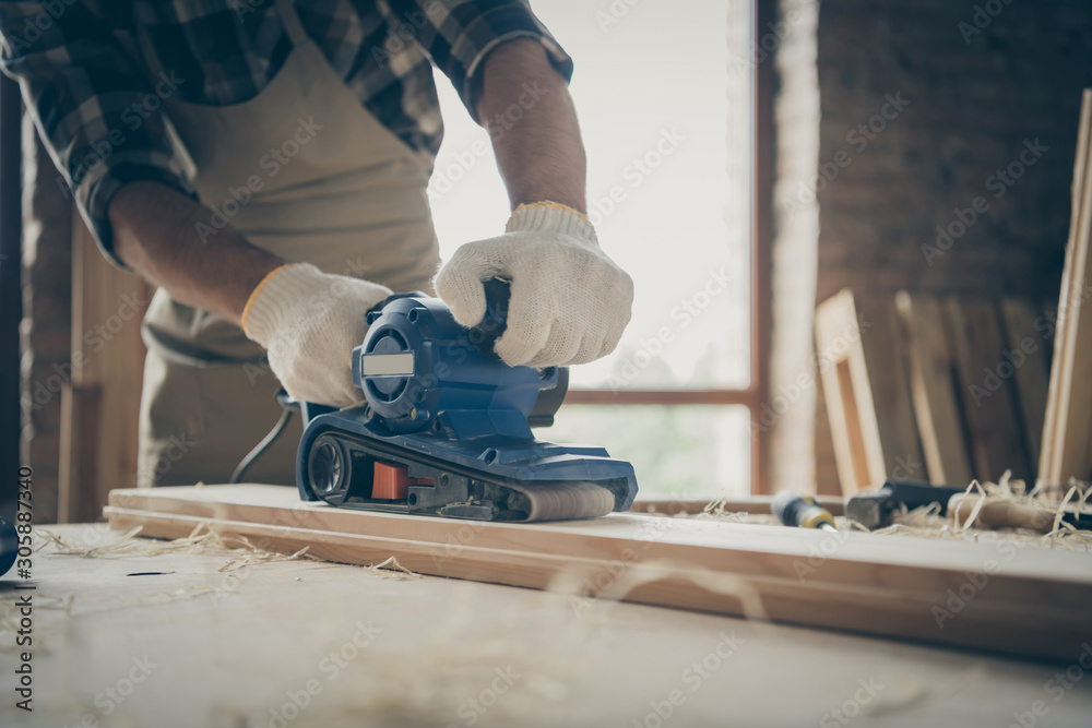 Cropped close up photo of man working with sandpaper surrounded with filings processing wooden block with hands in gloves Cropped close up photo of man working with sandpaper surrounded with filings processing wooden block with hands in gloves