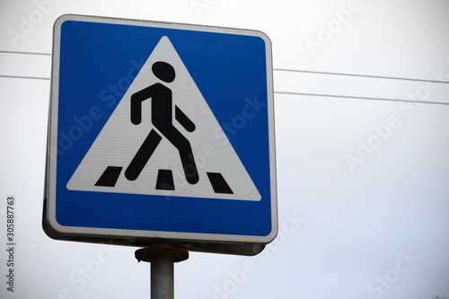 Blue road crossing sign on white sky background
