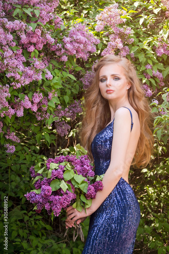 Portrait of young beautiful blonde woman posing among blooming lilac. Outdoor fashion photo of young woman surrounded by flowers. Spring blossom