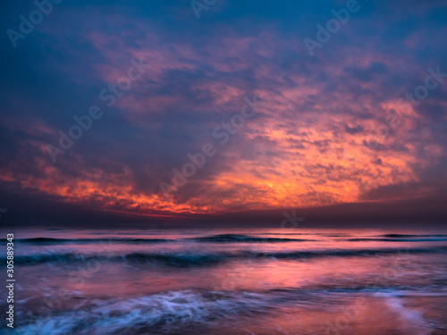 Beautiful orange dawn / sunrise over the Mediterranean Sea, waves splashing against the shore