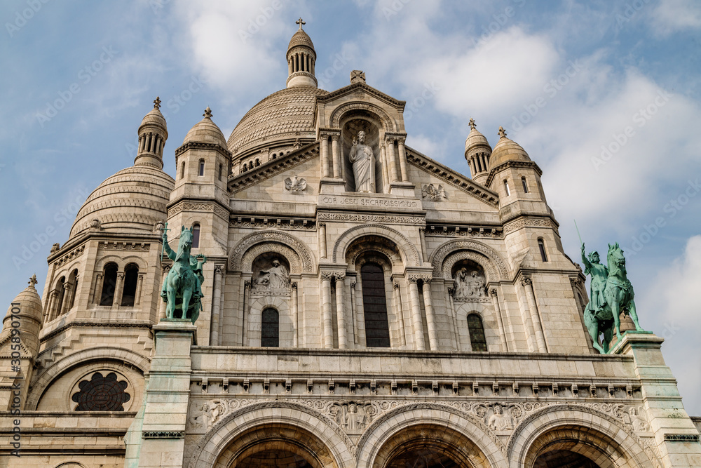 The Basilica of the Sacred Heart of Jesus known as Sacre-Coeur Basilica on Montmartre hill in Paris. Low angle view against blue clouded sky.