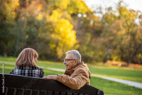 Romantic senior couple is sitting on bench in park and enjoying autumn.