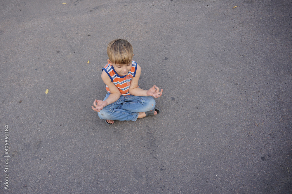 A boy is meditating sitting on the asphalt in the middle of the road. A boy is meditating sitting on the asphalt in the middle of the road.