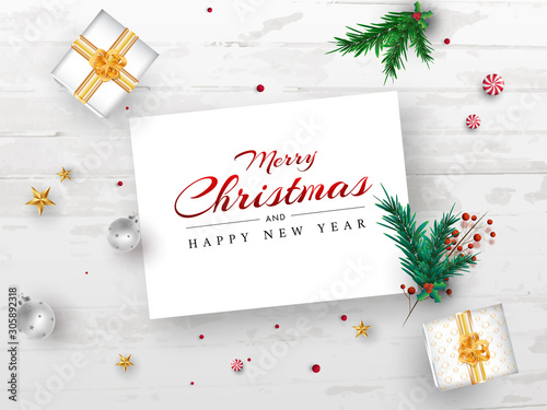 Merry Christmas and Happy New Year message card with pine leaves, red berries, star, baubles and gift boxes on white wooden texture background.