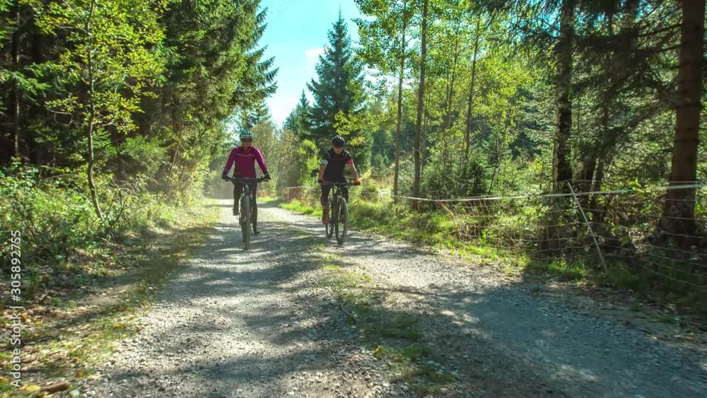 A couple, wearing protective gear and riding mountain bikes on the path amidst beautiful jungle.Front view.