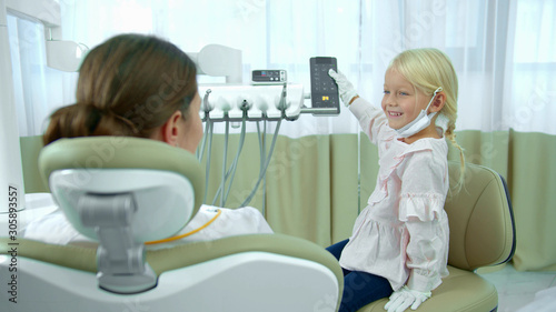 Girl regulates the chair where dentist is sitting.