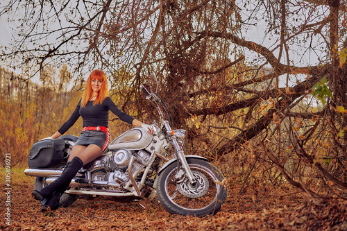 red-haired female biker in the autumn forest at sunset photo