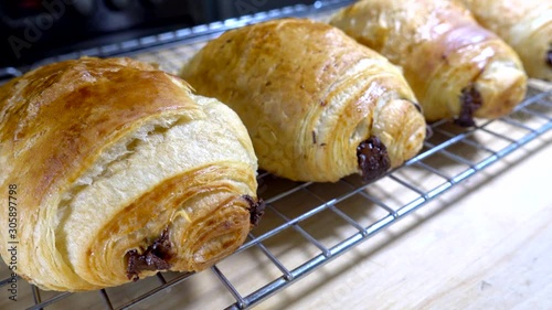 Closeup circular dolly shot of a row of oven baked pain au chocolat pastries / cholcolate croissants resting on a cooling grid. photo