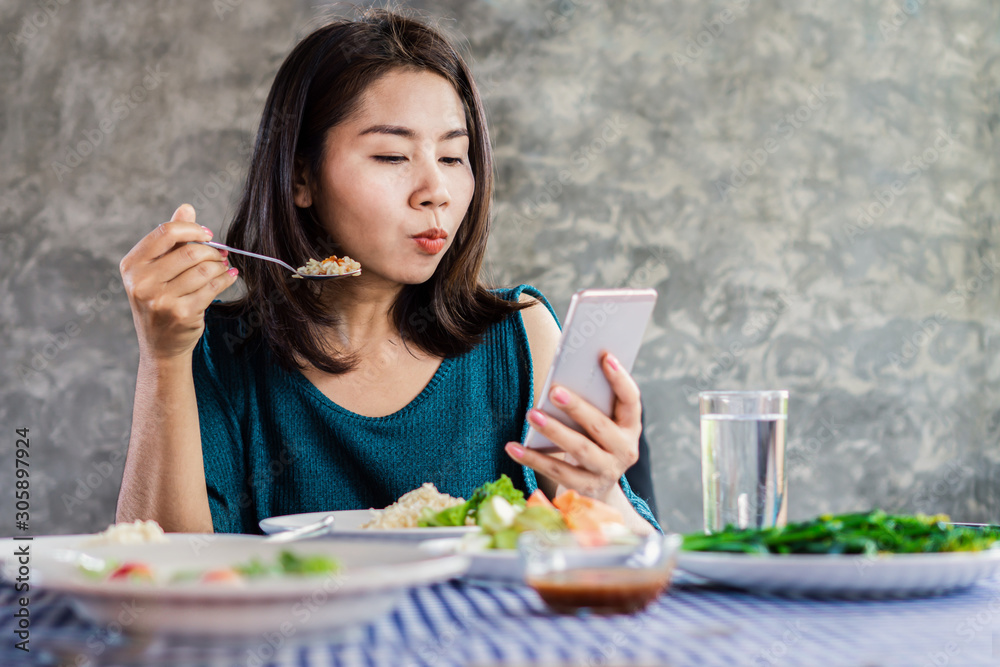 internet and social media addiction concept with Asian woman using mobile phone while eating dinner at home internet and social media addiction concept with Asian woman using mobile phone while eating dinner at home