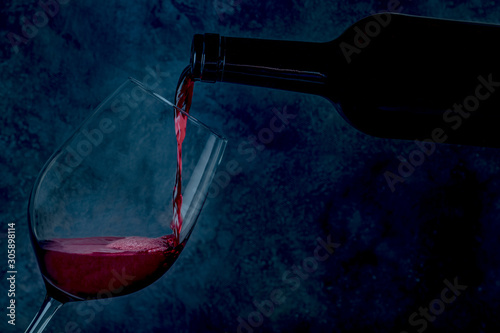 Wine poured into a glass from a bottle, on a dark background with copy space, toned image