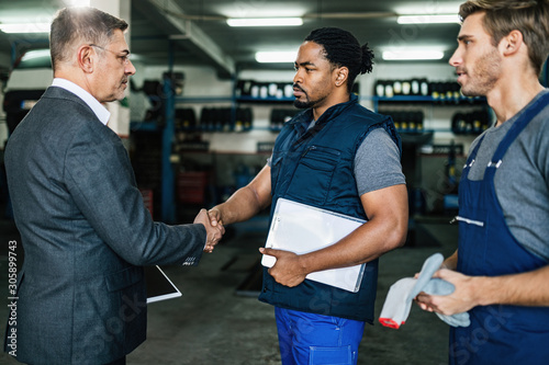 African American car mechanic shaking hands with a manager in auto repair shop.