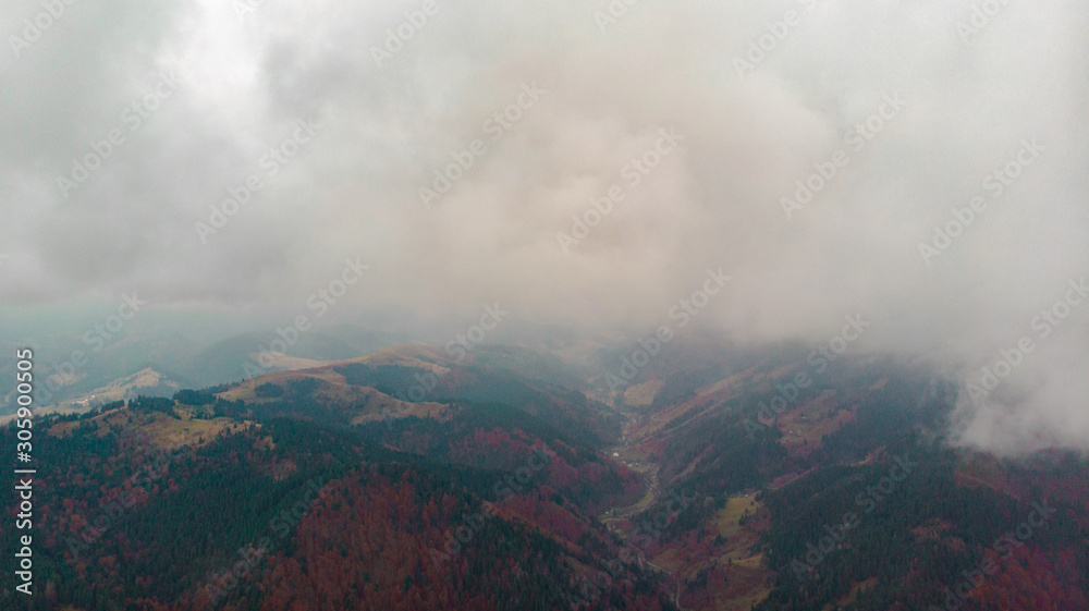 View from a drone to a glade and autumn forest through the fog in the Carpathian mountains.