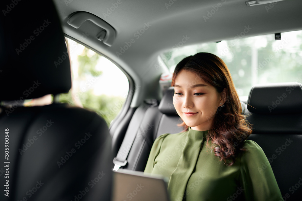 Beautiful businesswoman using laptop while sitting on a backseat of a car.