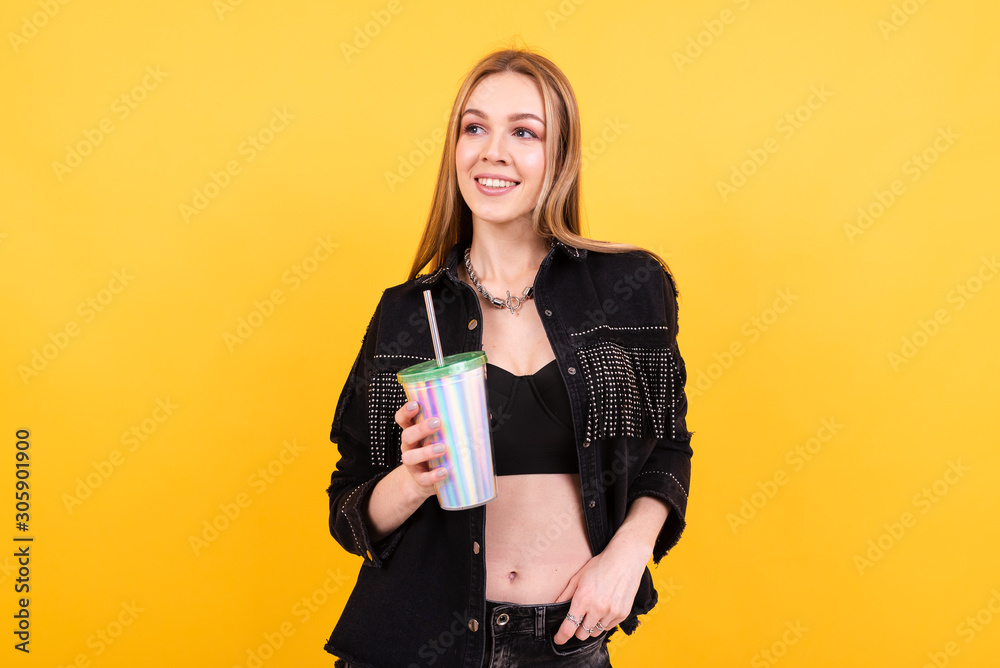 Young beautiful girl drinks cocktail on yellow background