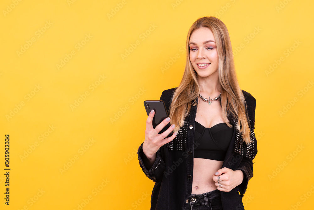 Young beautiful girl in black clothes with phone on yellow background, business woman